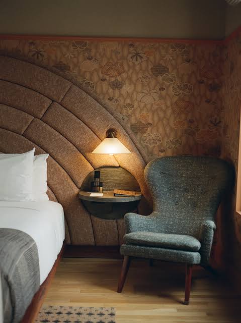 Guestroom nap alcove at Santa Monica Proper: arched upholstered headboard, warm shaded lamp and a tweed armchair