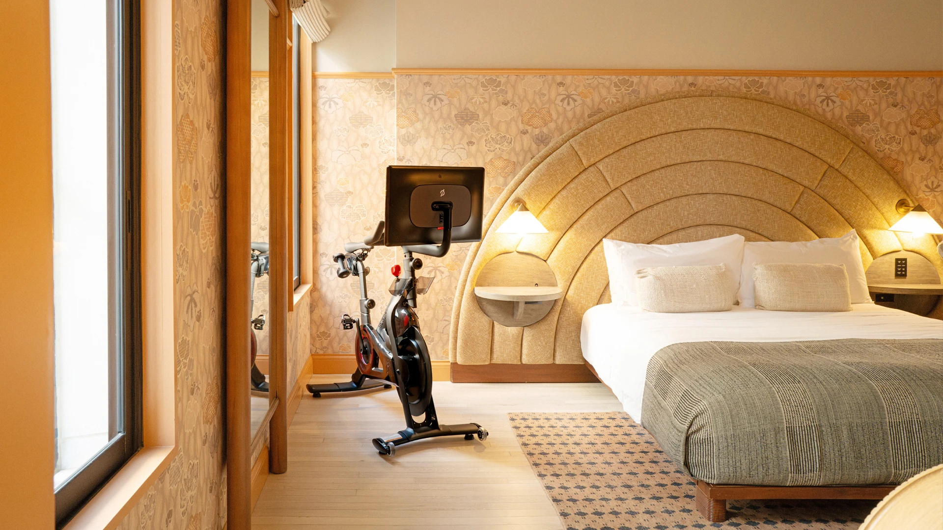 Performance wellness room with a Peloton bike beside the arched upholstered headboard and king bed