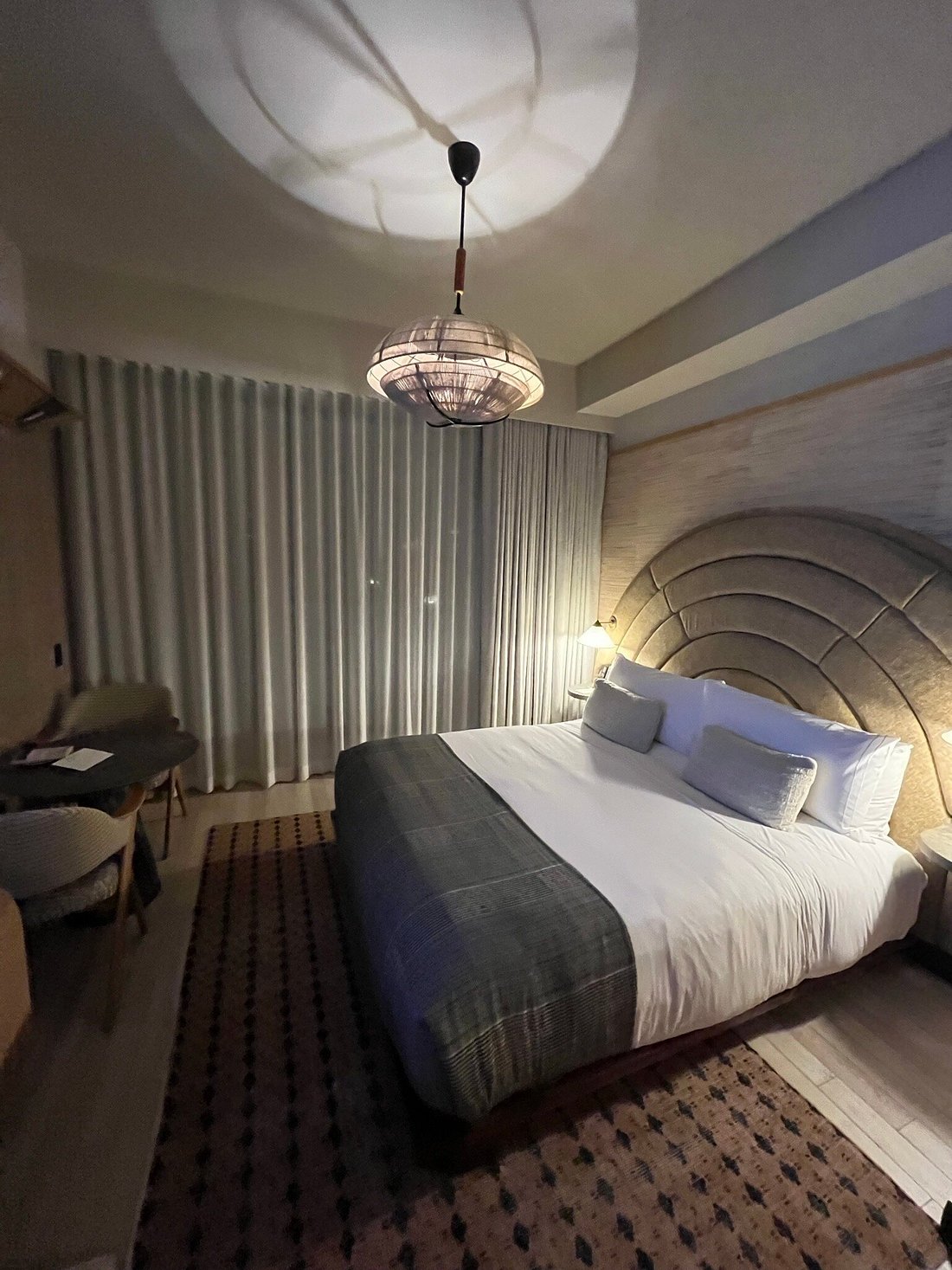 Dimly lit Santa Monica Proper guestroom at night with an arched headboard and woven pendant light